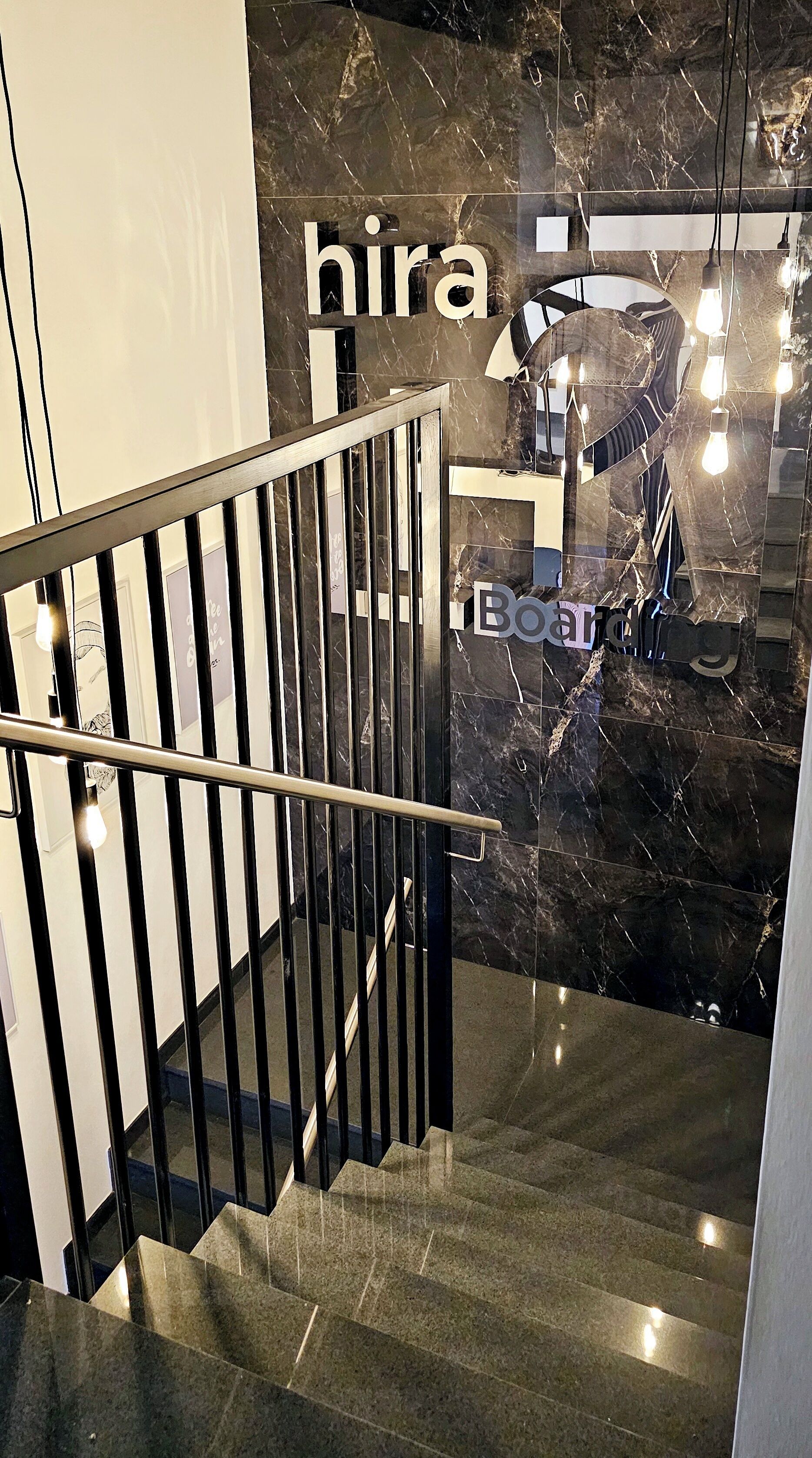 Una escalera moderna con barandilla metálica que conduce a una habitación con pared de mármol oscuro y un letrero que dice "hira".