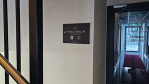 A sign indicating a self-service washroom with a shower and toilet, and a staircase with black and gold railings. - Hira Boarding Aparthotel (Dingolfing)