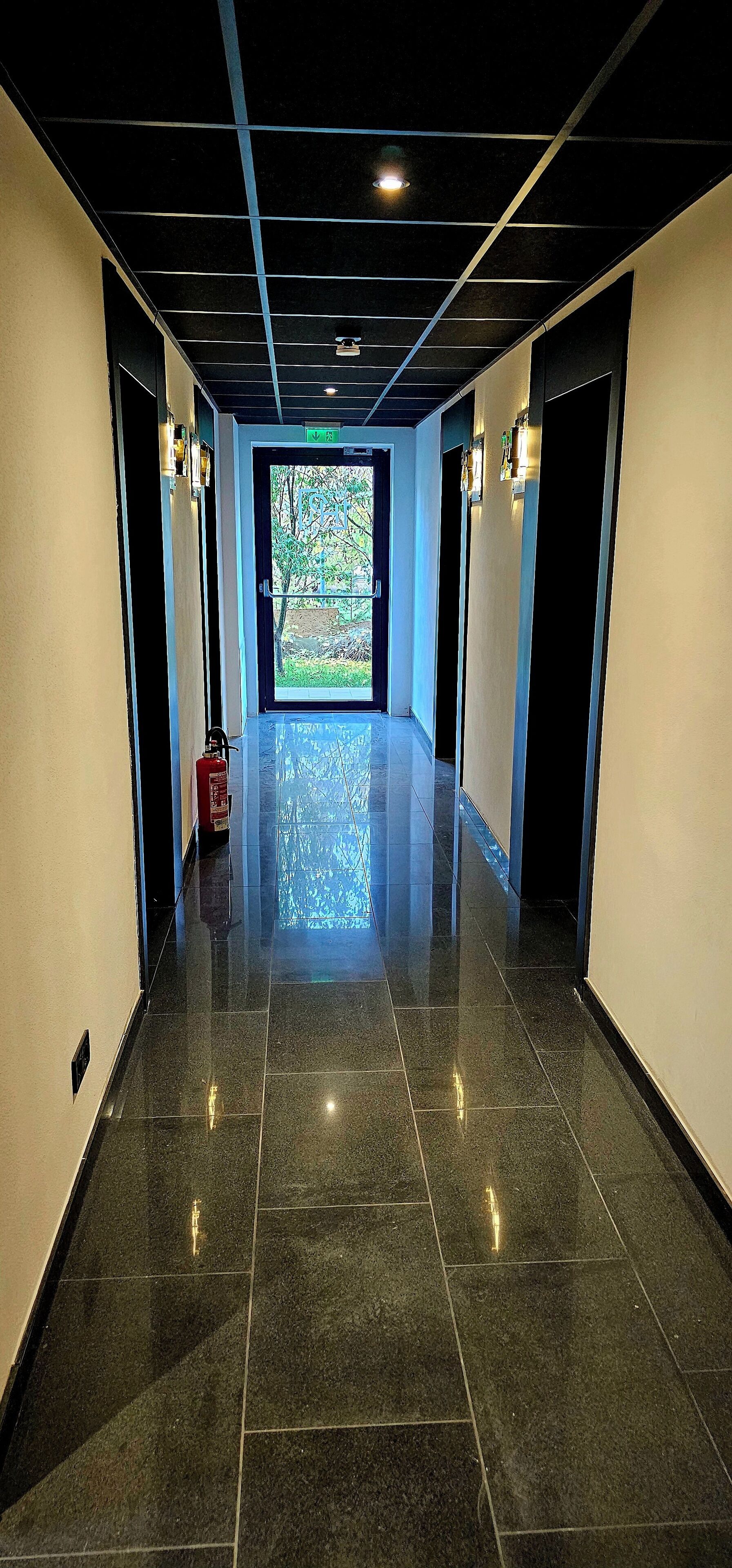 A hallway with a polished tile floor, recessed lighting, and doors on both sides.