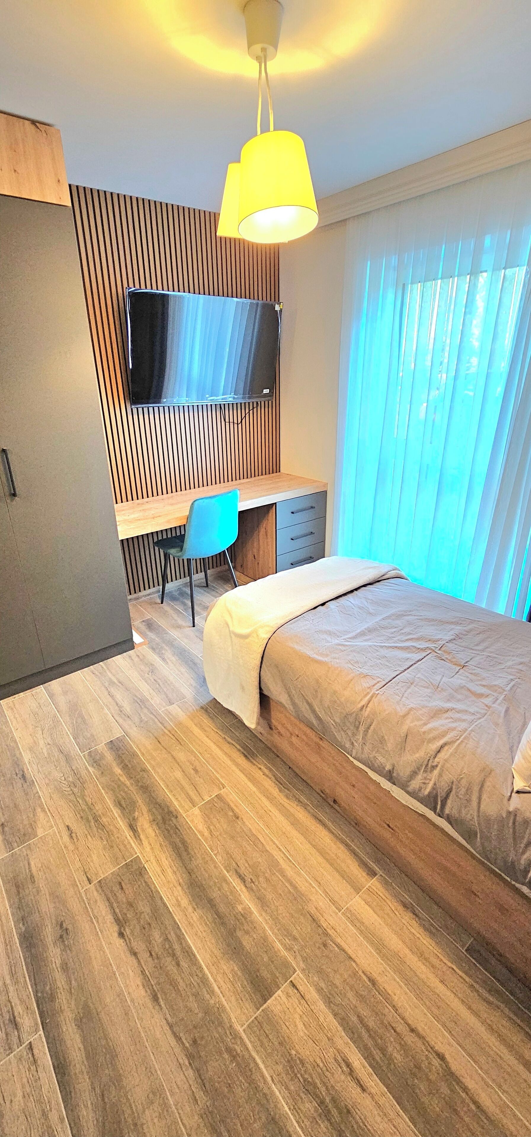 Un dormitorio moderno con una cama, un escritorio, una silla y un televisor montado en una pared de madera.