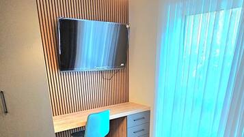 Un dormitorio moderno con una cama, un escritorio, una silla y un televisor montado en una pared de madera.