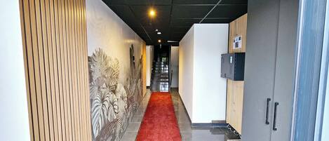 Un pasillo con alfombra roja, una pared con diseño de hojas y una escalera que sube a un nivel superior.