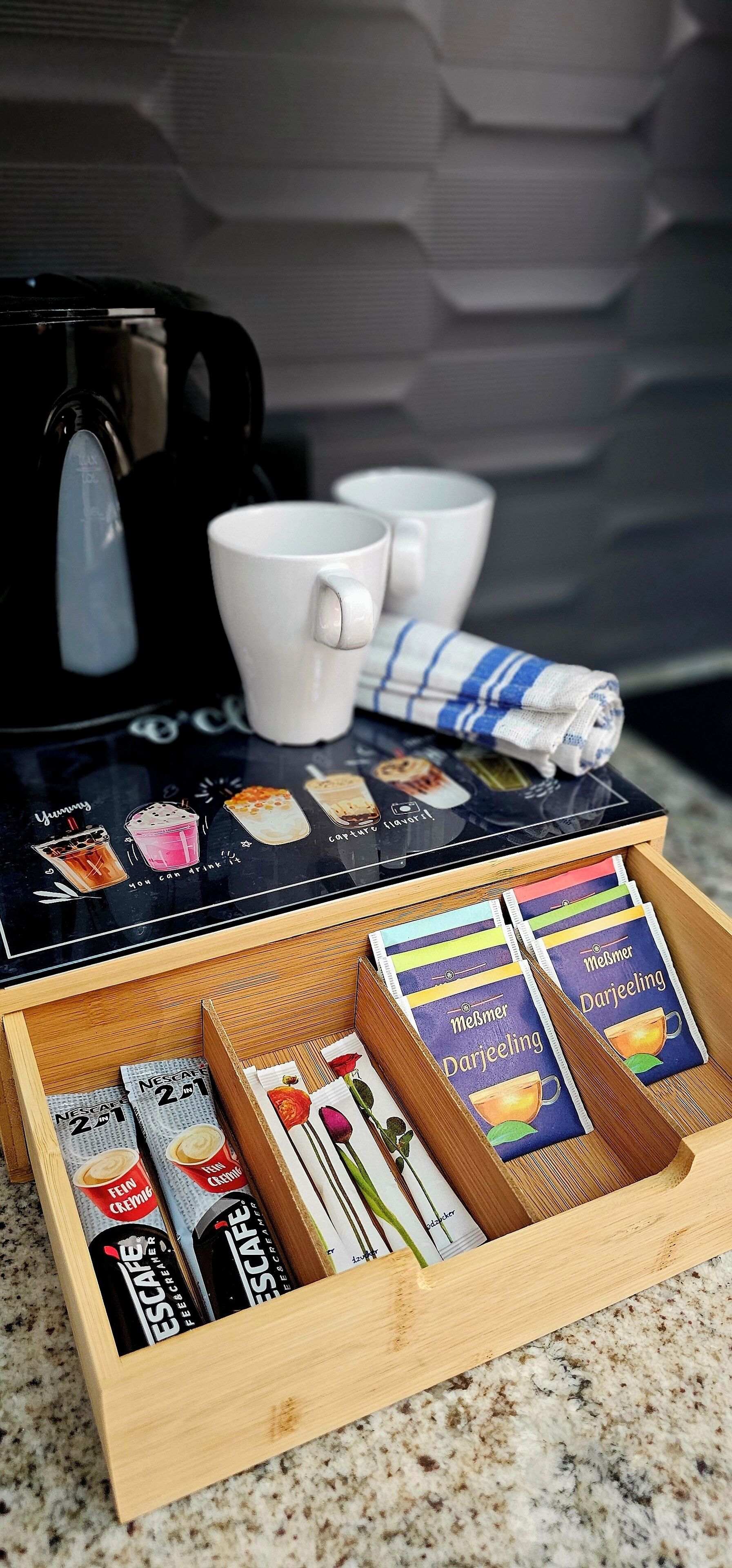 Una estació de cafè amb una cafetera, tasses i una safata amb sobres de cafè i una tovallola.