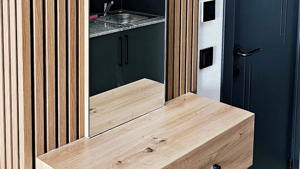 A modern kitchen with a built-in wooden cabinet, a countertop with a sink, and a dark-colored door. - Hira Boarding Aparthotel (Dingolfing)