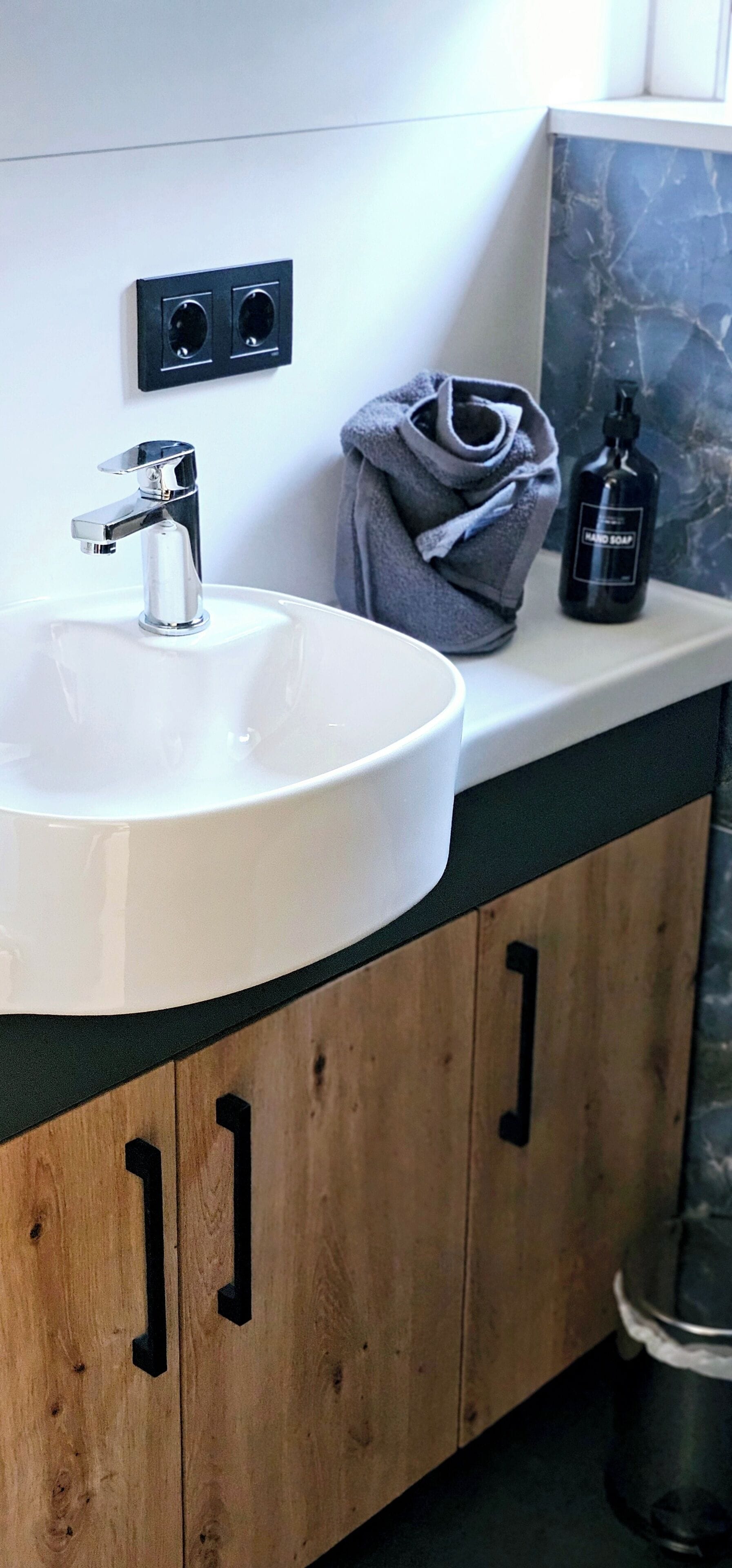 A bathroom with a white sink, wooden cabinets, a towel, and a bottle of hand soap.