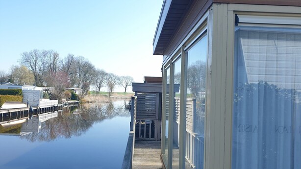A waterfront property with a dock, a covered walkway, and a large window overlooking a calm body of water. - Luxury Holiday Home in Bantega With Harbour and Sloop (Bantega)