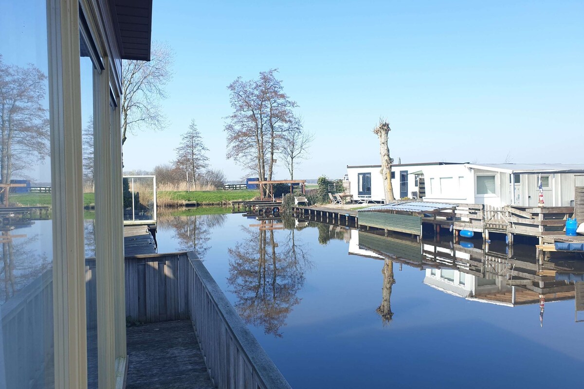 A calm water body with a wooden dock, a modern house, and a clear sky.