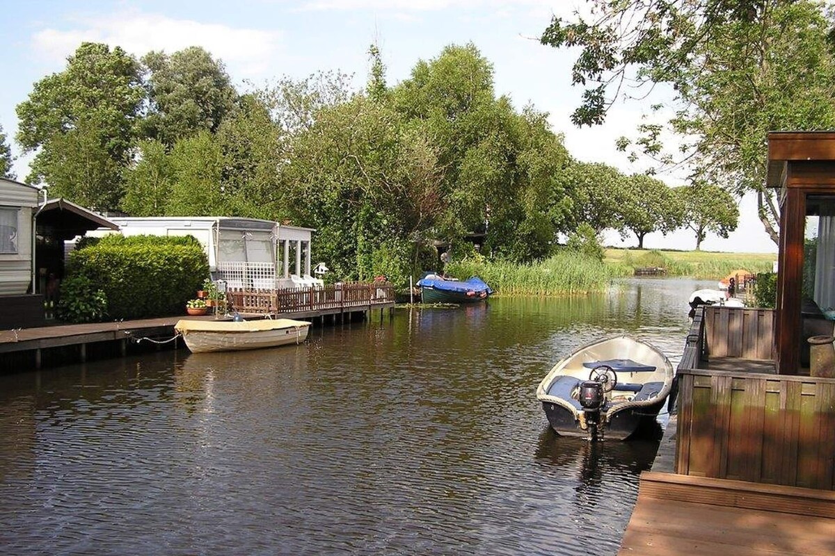A calm river with boats docked at wooden piers, surrounded by lush greenery and trees.
