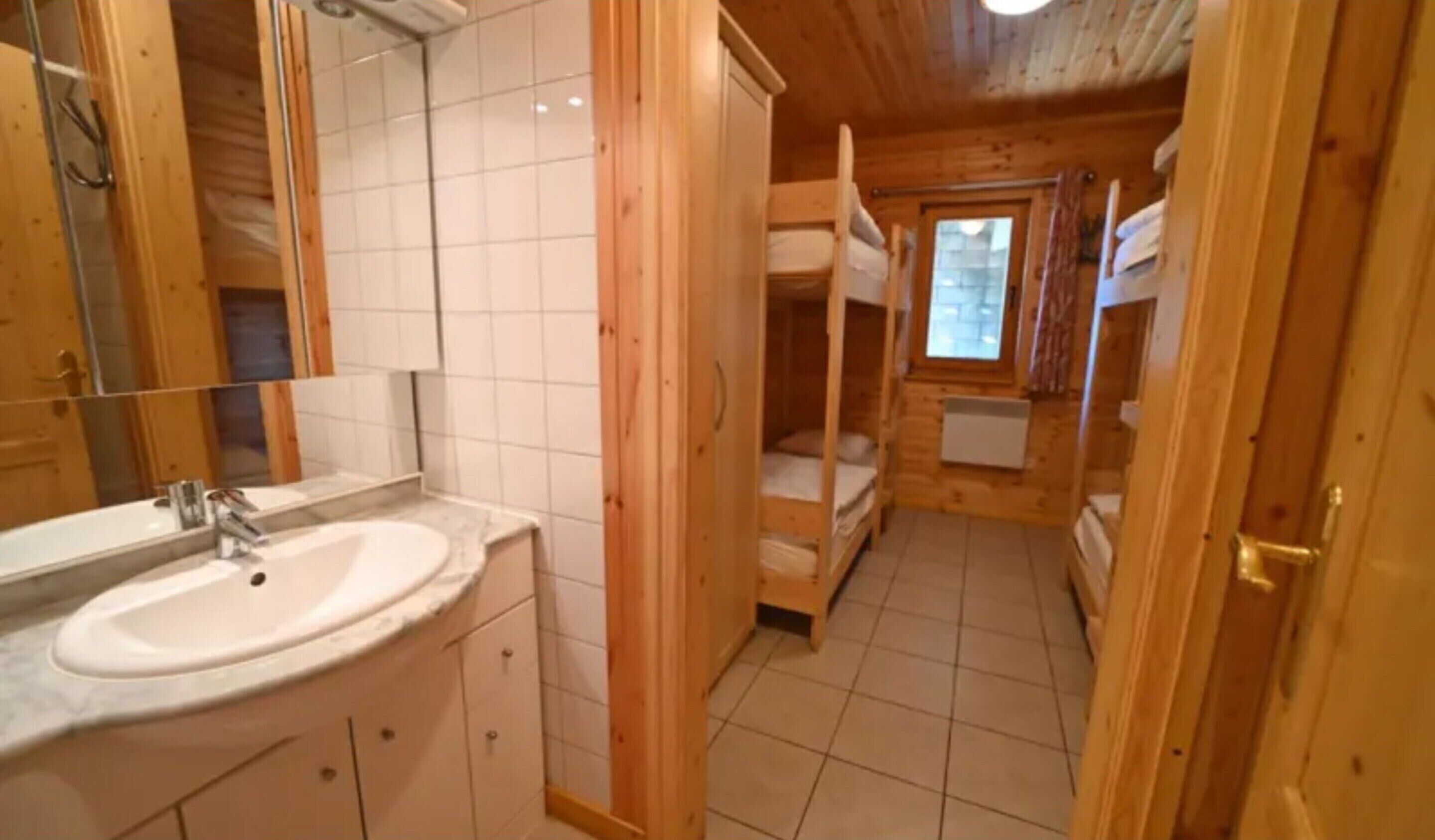 A wooden cabin interior with a bathroom featuring a sink, mirror, and tiled floor.