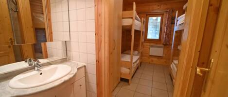 A wooden cabin interior with a bathroom featuring a sink, mirror, and tiled floor.