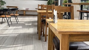 A modern cafe interior with wooden tables and chairs, a chalkboard menu, and large windows offering views of the city. - Easy Stay at Embassy Gardens Apartment (Accra)