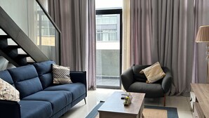 A modern living room with a blue sofa, a grey armchair, and a wooden coffee table. - Easy Stay at Embassy Gardens Apartment (Accra)