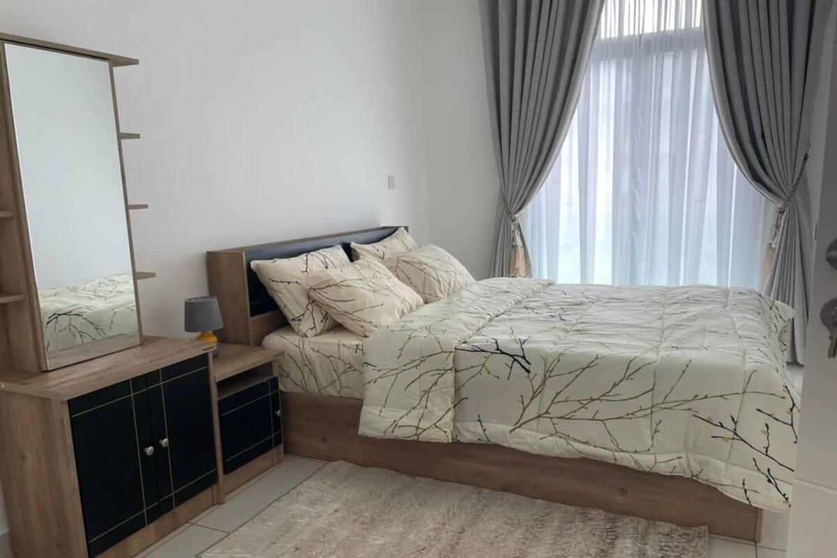 A bedroom with a bed, a dresser, a mirror, and a window with curtains.