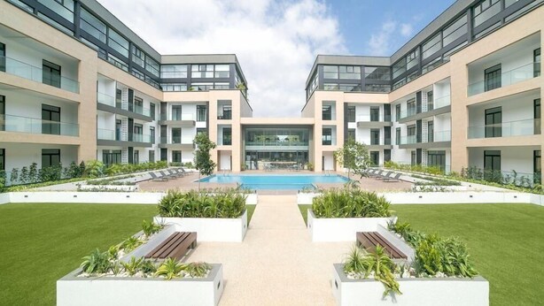 A modern building with a central courtyard featuring a swimming pool, surrounded by greenery and seating areas. - Easy Stay at Embassy Gardens Apartment (Accra)
