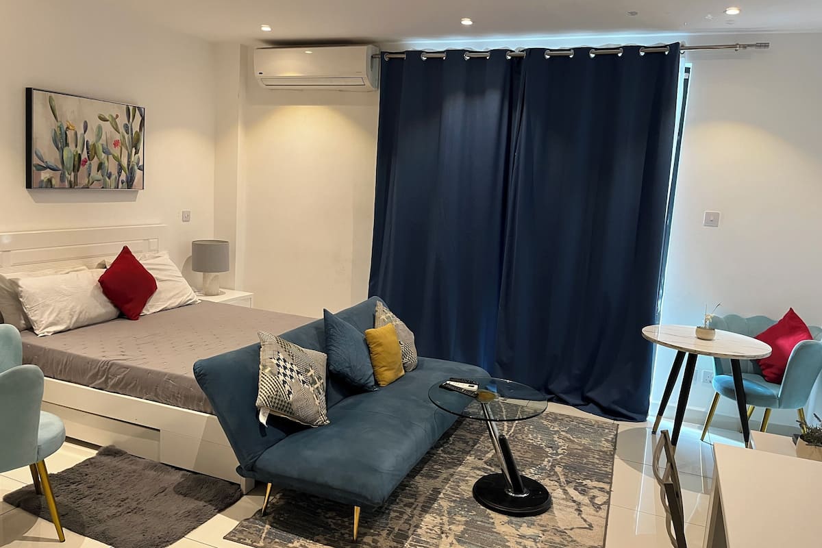 A modern bedroom with a bed, a blue sofa, a small round table, and a painting on the wall.