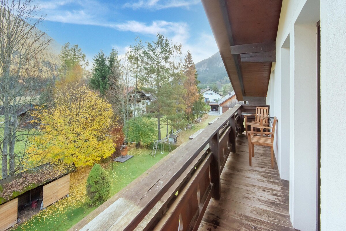 Un balcon donnant sur une pelouse verdoyante, des arbres et des maisons en arrière-plan.