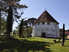 A white building with a conical roof, surrounded by trees and grass.