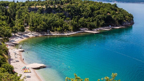 Et kystområde med strand, klart turkis vand og en skovklædt bakke.