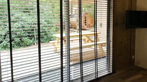 A room with a large window with horizontal blinds, a wooden floor, and a television mounted on the wall. - Lush Holiday Home in Rheezerveen With Hot Tub (Rheezerveen)
