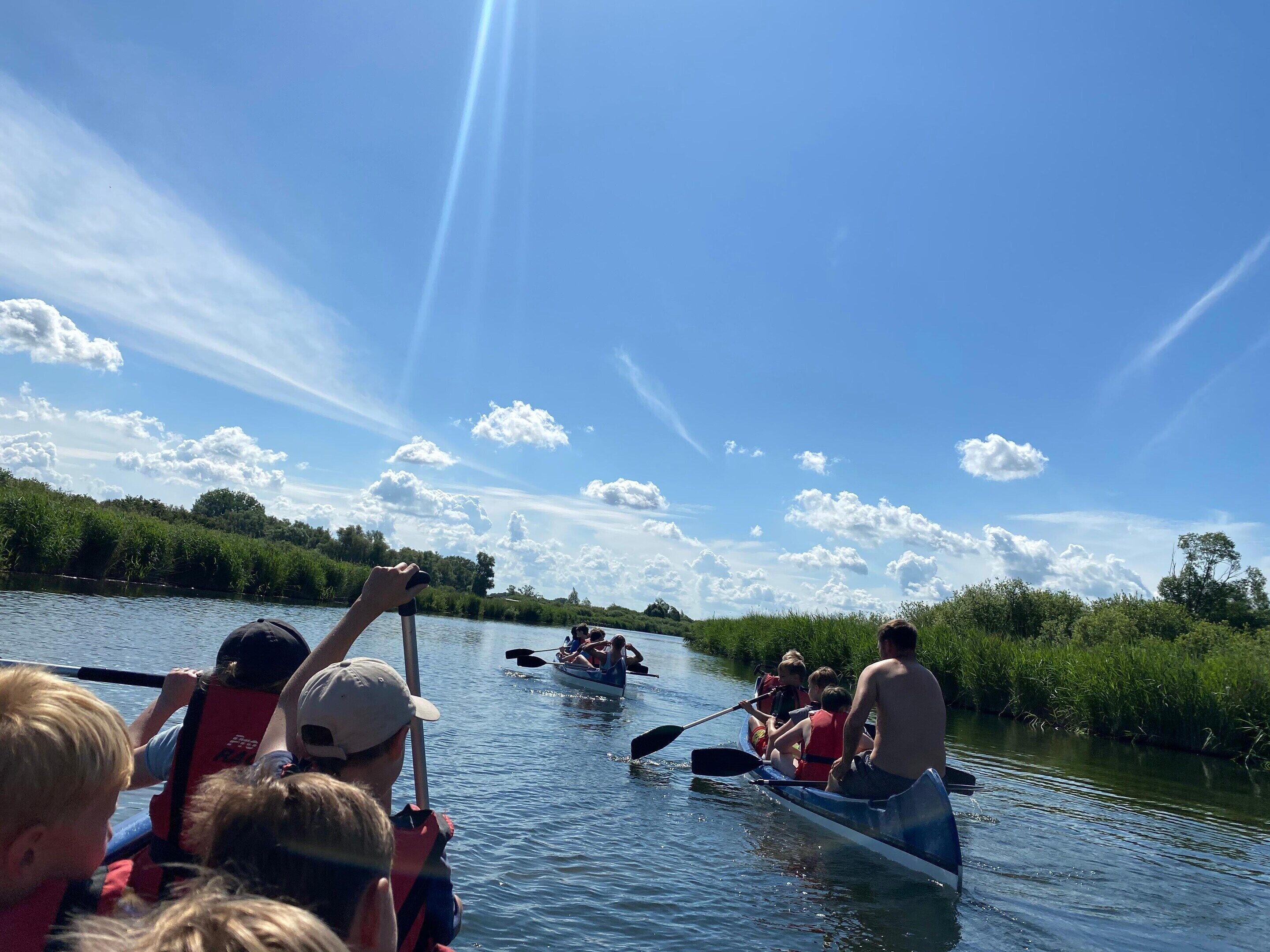 A group of people in a canoe on a river, with a clear sky and greenery in the background.