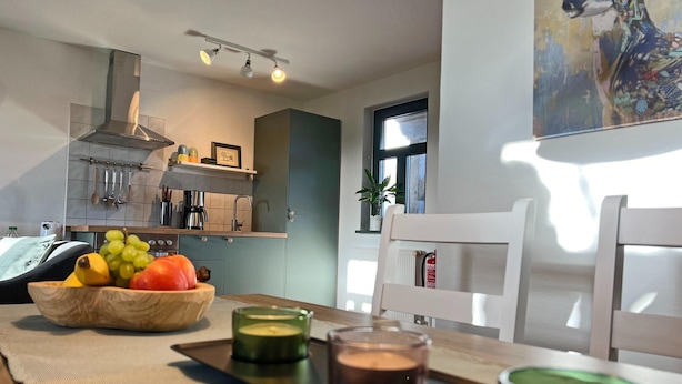 Moderni keittiö, jossa on ruokailutila, hedelmäkulho, kynttilöitä ja taulu.