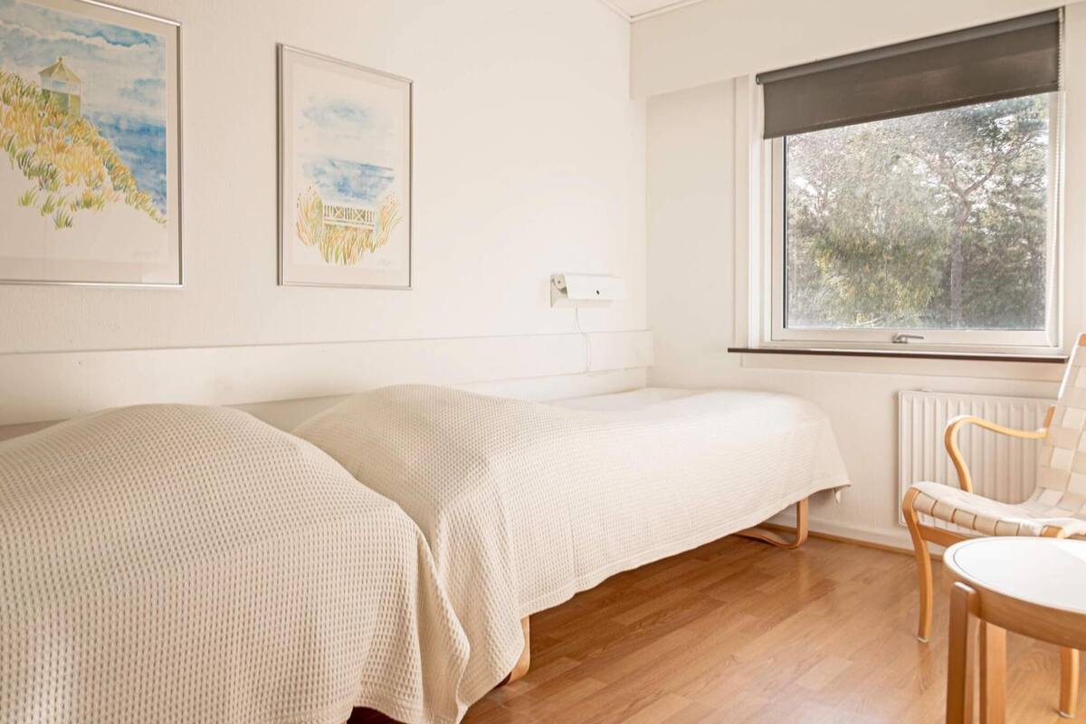 A room with two single beds, a wooden floor, a window with a view of trees, and a chair.