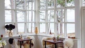 A cozy room with large windows overlooking a body of water, furnished with white chairs and tables, and decorated with natural elements like a vase of flowers and a woven lamp. - 6 Person Holiday Home on a Holiday Park in Gilleleje (Gilleleje)