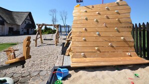 Eine Spielanlage aus Holz mit einer Flagge, einer Schaukel und einer hölzernen Bank in einem Innenhof.