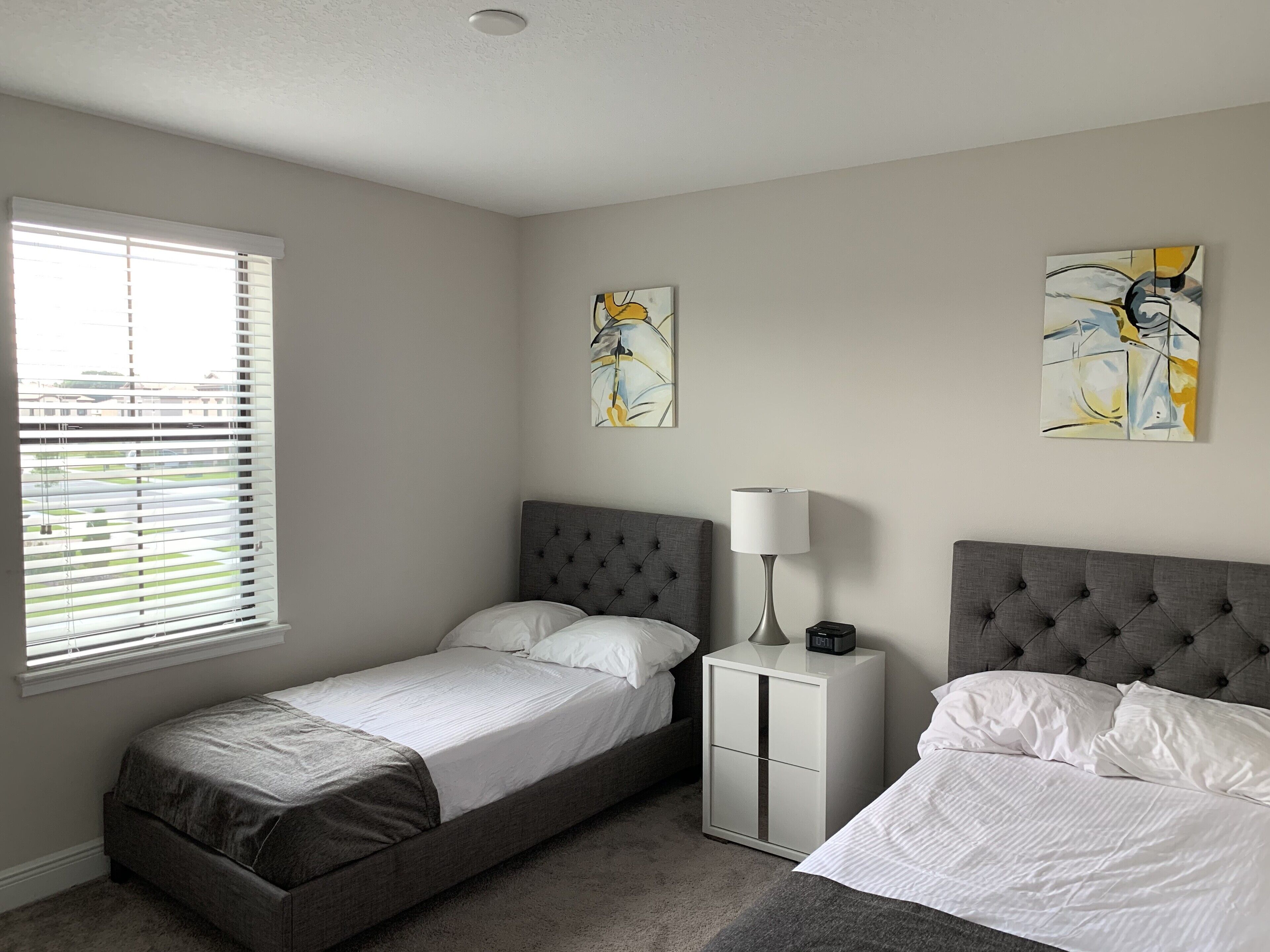 A bedroom with two beds, a nightstand, a lamp, and artwork on the walls.