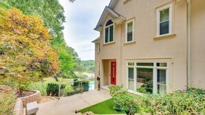 A two-story house with a red door, a balcony with a glass railing, and a well-maintained garden with various plants and shrubs. - Modern Retreat w/ River View in Roswell! (Roswell)