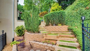 A landscaped garden with a stone retaining wall, wooden steps, and a metal fence. - Modern Retreat w/ River View in Roswell! (Roswell)
