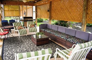 Un espacio patio al aire libre con mobiliario de mimbre, una parrilla y un tapete estampado.