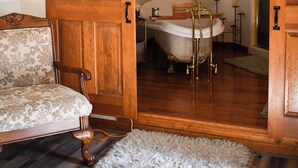 A room with a wooden door, a vintage chair, a bathtub, and a mirror on the wall. - Merrily Yours! (Fortville)