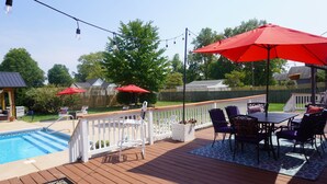 A wooden deck with a pool, outdoor furniture, and red umbrellas. - Merrily Yours! (Fortville)