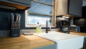 Une cuisine avec un évier blanc, une machine à café et une fenêtre donnant sur des arbres.