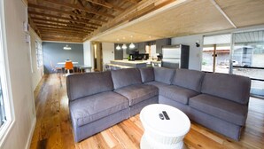 Un salon moderne avec un grand canapé d’angle, une table basse ronde et un coin cuisine à l’arrière-plan.
