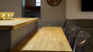 Une table à manger en bois avec des chaises, une horloge murale et un téléviseur fixé au mur.