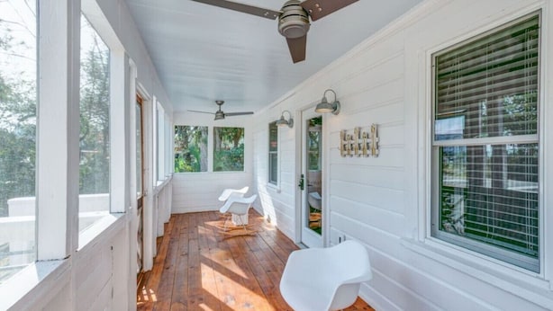 A covered porch with wooden flooring, white walls, and ceiling fans.