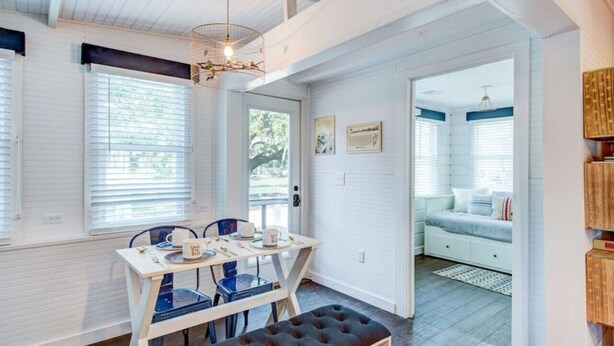 A bright room with a dining table, chairs, and a bench. There is a door leading to another room with a bed. - Authentic 1940's renovated Folly cottage! (Charleston)