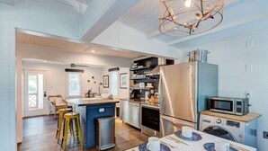 A modern kitchen with a central island, stainless steel appliances, and a dining area set for six. - Authentic 1940's renovated Folly cottage! (Charleston)