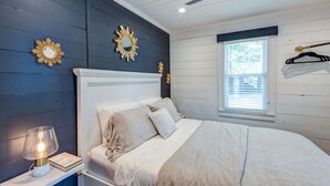 A bedroom with a bed, a nightstand with a lamp, a ceiling fan, and a window with blinds. - Authentic 1940's renovated Folly cottage! (Charleston)