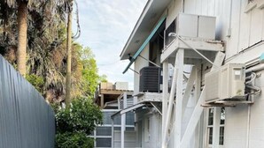A narrow pathway leading to a building with a grey fence on one side and a white exterior. - Studio- Behind Bert’s Market (Folly Beach)