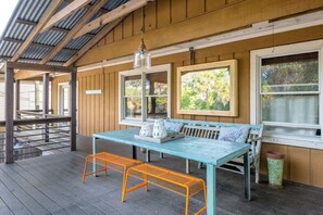A covered outdoor seating area with a table and benches, framed windows, and a hanging light fixture.
