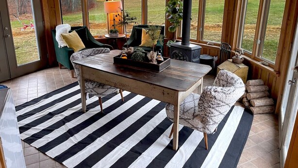 Een gezellige kamer met een houten tafel, een gestreept vloerkleed en grote ramen met uitzicht op de omgeving.
