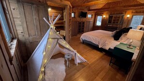 Een gezellig chaletinterieur met een bed, een tafeltje, een lamp en een tipitent met verlichting.