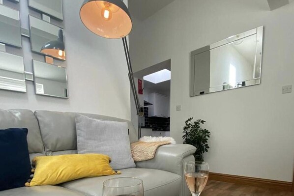 A modern living room with a grey sofa, a floor lamp, a mirror, and a potted plant.