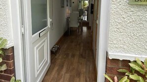 Un couloir étroit au plancher de bois, une porte sur la gauche et une petite table avec un bol sur la droite.