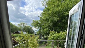 Un balcon doté d’un sol en pierre, de plantes en pot et offrant une vue sur un jardin et une maison situés au loin.