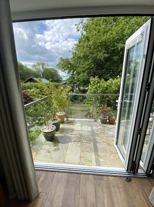 A balcony with a stone floor, potted plants, and a view of a garden and house in the background.