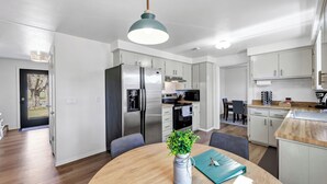 A modern kitchen with stainless steel appliances, a dining area with a wooden table, and a view of the outdoors. - Walk to Lambeau! Sleeps 8• Fire Pit • Party Garage • Parking for 6 vehicles (Ashwaubenon)